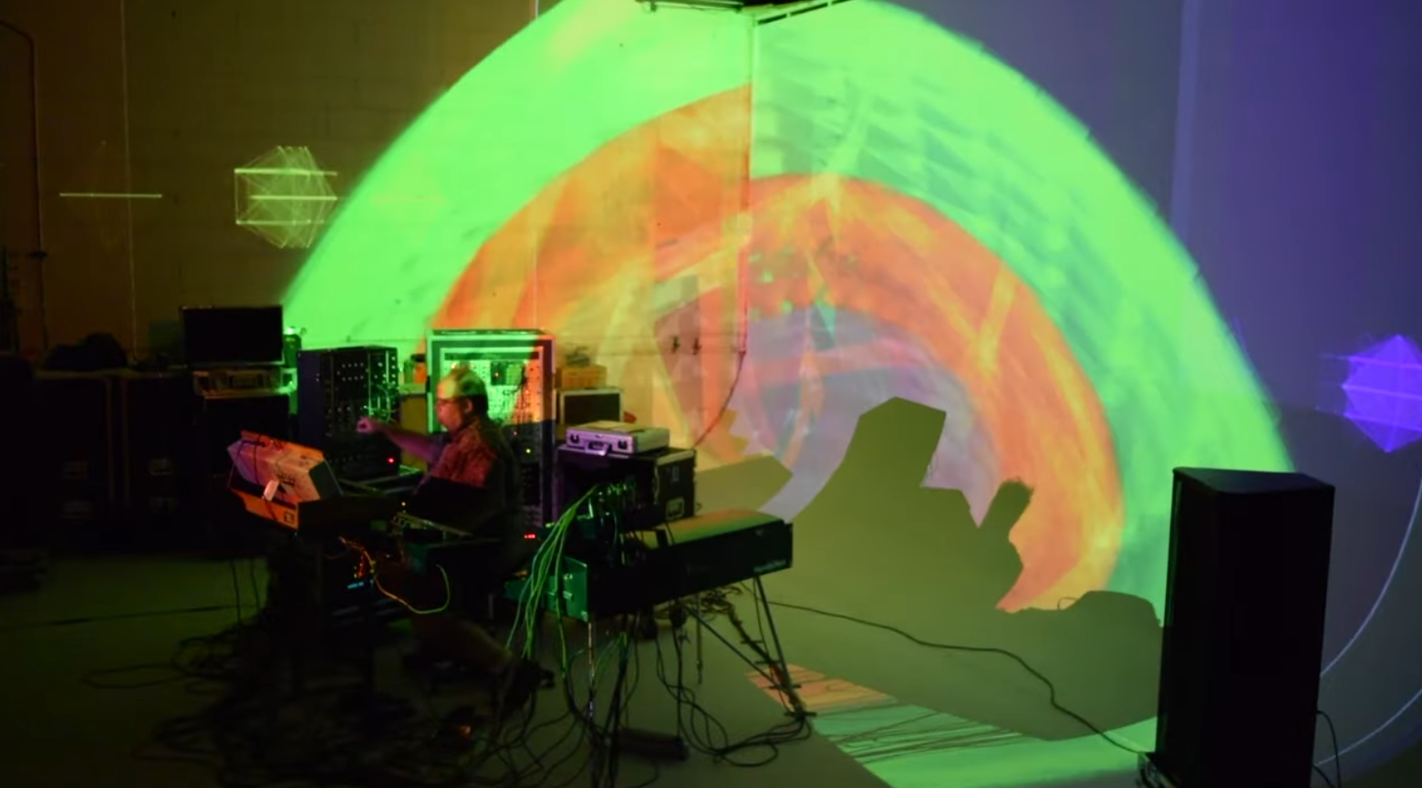 Mike Olson performance setup with large green and orange projection mapped visuals